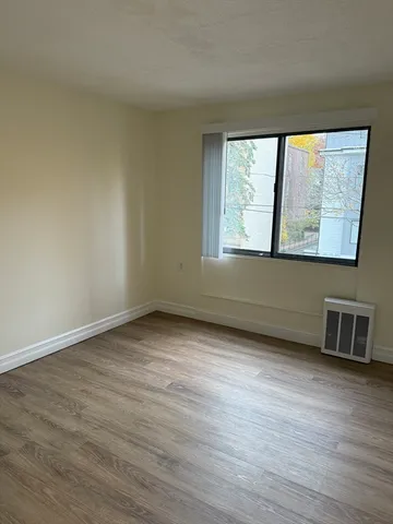 a view of an empty room with wooden floor and a window
