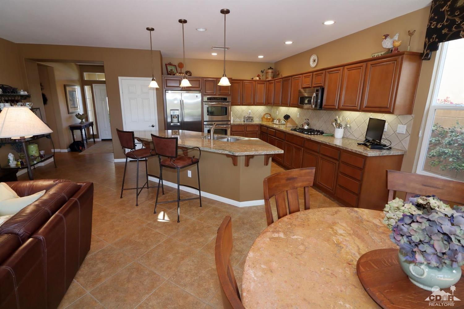 81757 Rustic Canyon Drive La Quinta, CA 92253 - Photo 16 of 40 a kitchen with stainless steel appliances kitchen island granite countertop a table chairs and a refrigerator