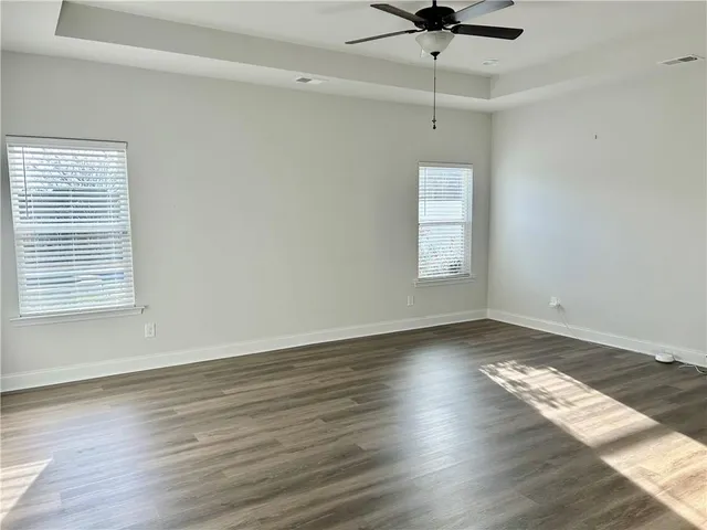 an empty room with wooden floor chandelier fan and windows