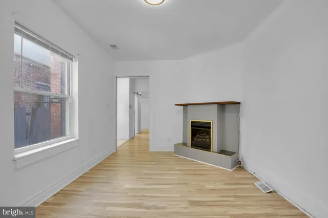 a view of an empty room with wooden floor fireplace and a window