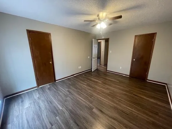a view of an empty room with wooden floor and a ceiling fan