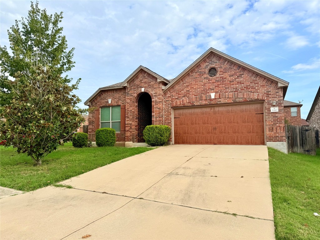 View of front of home with brick siding, driveway, a front lawn, and a garage