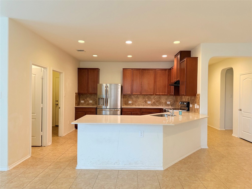 1140 Yellow Iris Road Leander, TX 78641 - Photo 4 of 23 Kitchen featuring arched walkways, stainless steel fridge, decorative backsplash, brown cabinets, and recessed lighting