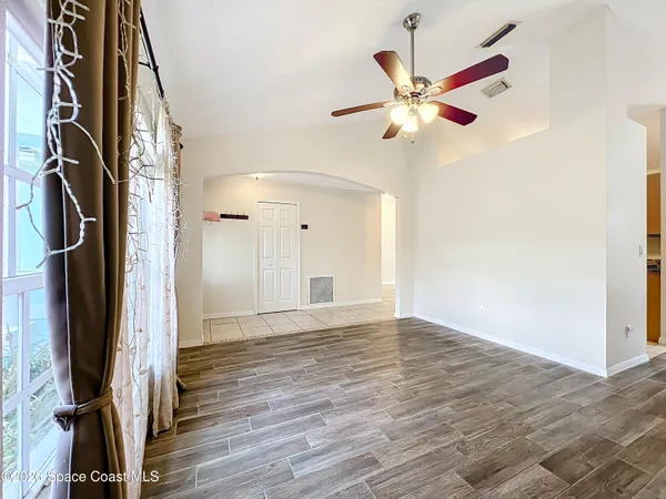 a view of an empty room with wooden floor and a ceiling fan