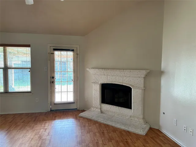 an empty room with wooden floor fireplace and windows