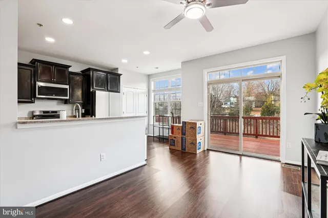 a living room with stainless steel appliances kitchen island granite countertop a stove a refrigerator a dining table and chairs with wooden floor