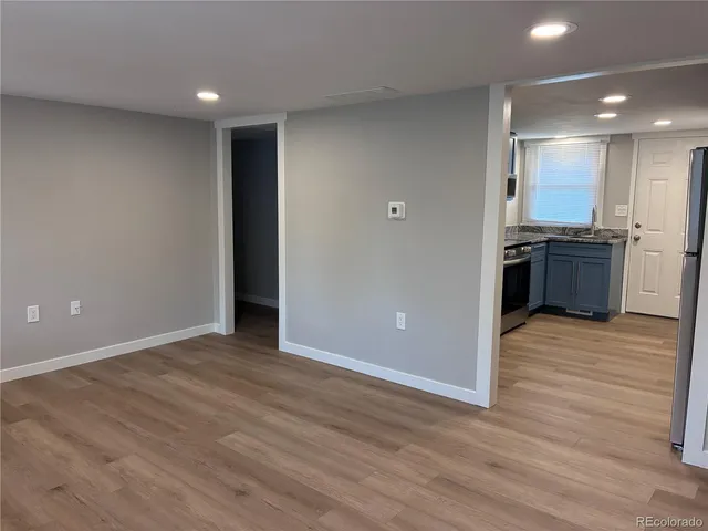an empty room with wooden floor and kitchen