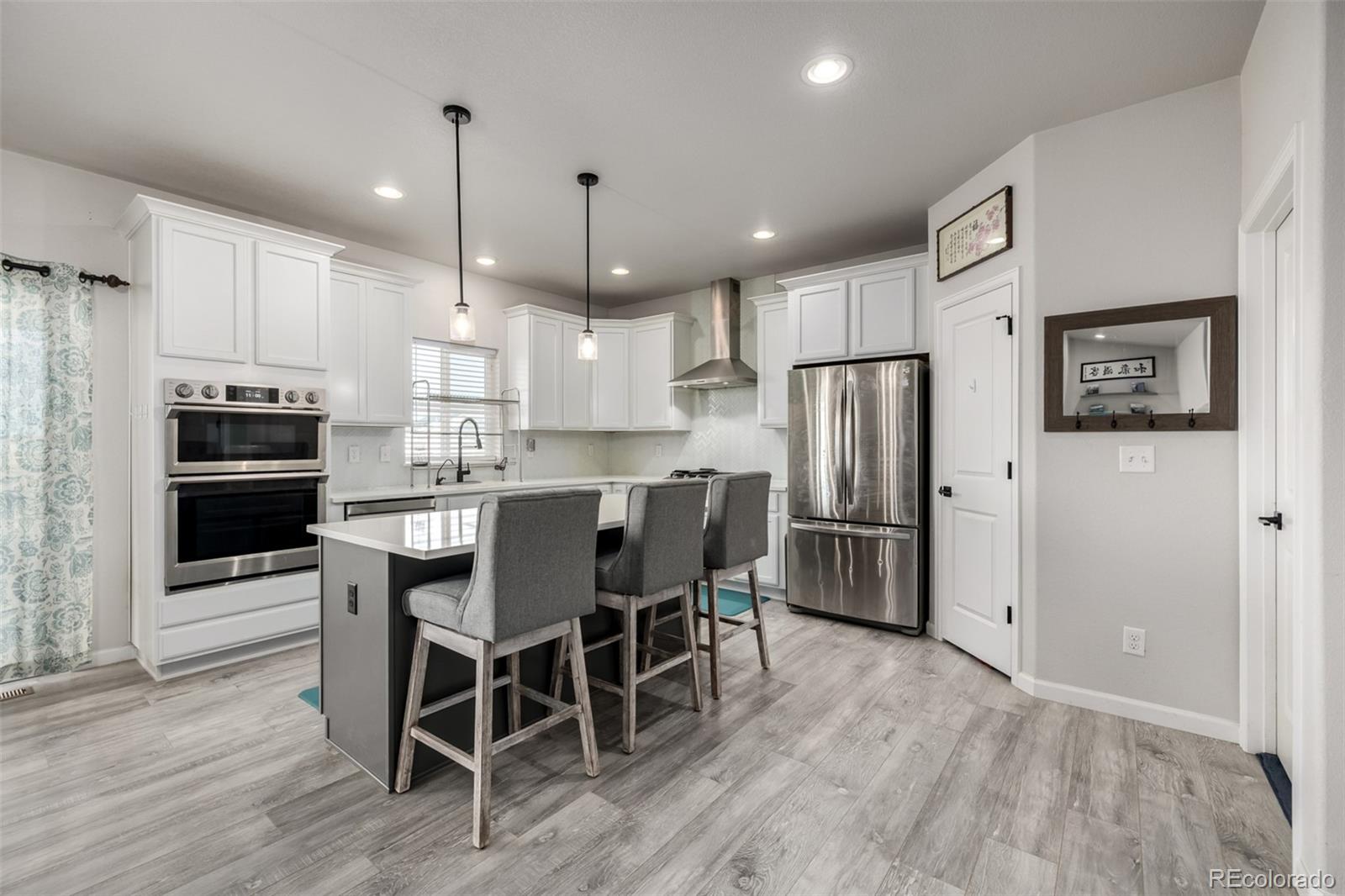 1875 Rancher Drive Milliken, CO 80543 - Photo 7 of 50 a kitchen with stainless steel appliances kitchen island granite countertop a refrigerator a stove a microwave oven a sink with island and chairs with wooden floor
