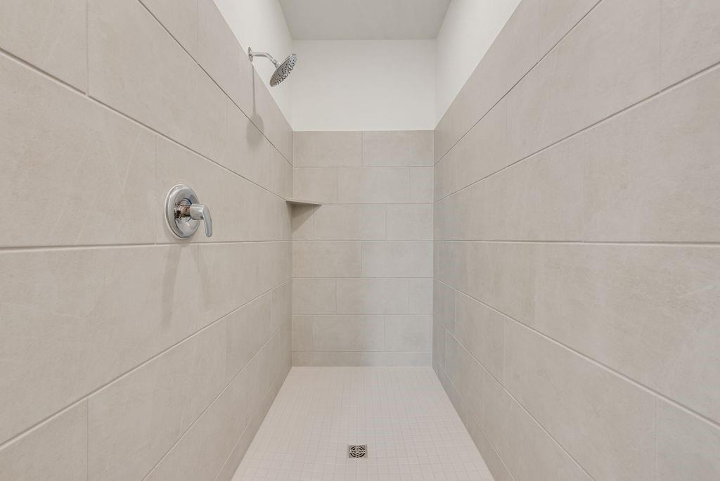 3009 Dutch Road Providence Village, TX 76227 - Photo 17 of 19 Walk-in shower featuring large format light-toned wall tiling, a built-in shower niche, and a chrome shower head with a single-handle control
