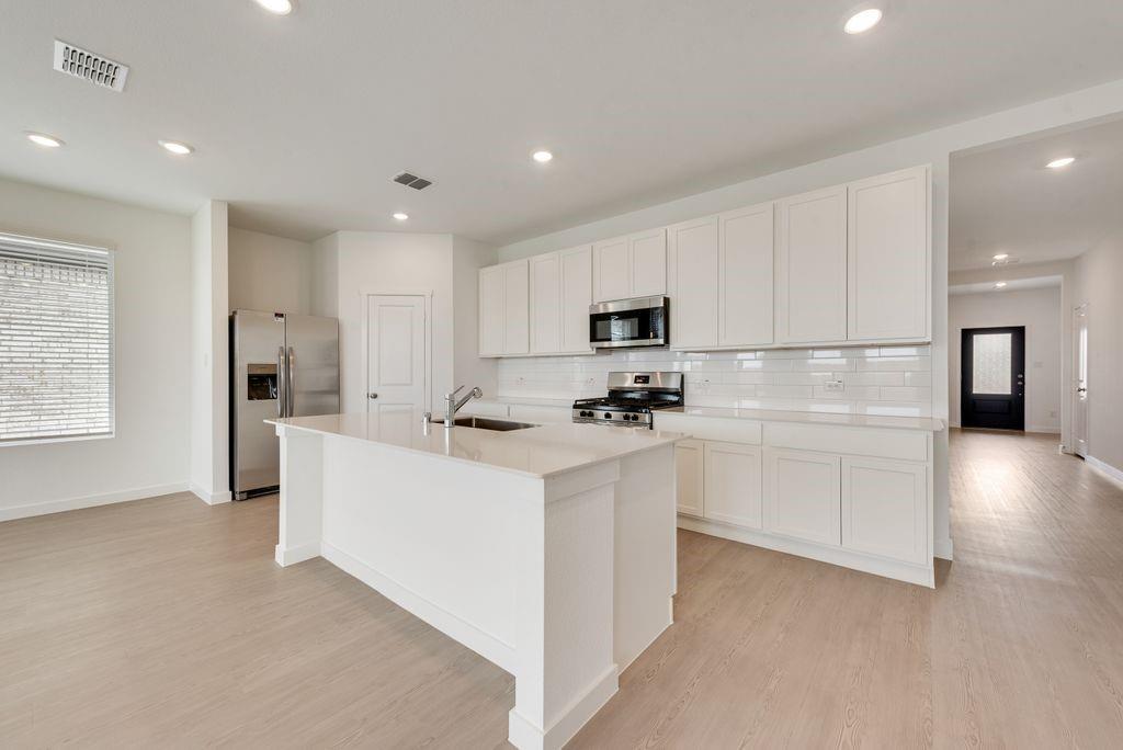 3009 Dutch Road Providence Village, TX 76227 - Photo 6 of 19 Open-concept kitchen featuring an island with a sink, white cabinetry, stainless steel appliances, and wood-finish flooring