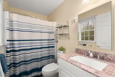 a bathroom with a granite countertop sink a toilet a mirror and shower curtain