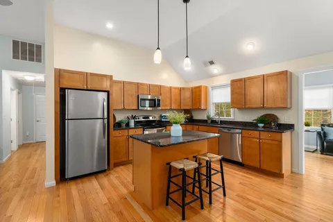 a kitchen with stainless steel appliances granite countertop a refrigerator a sink dishwasher a stove and white cabinets with wooden floor