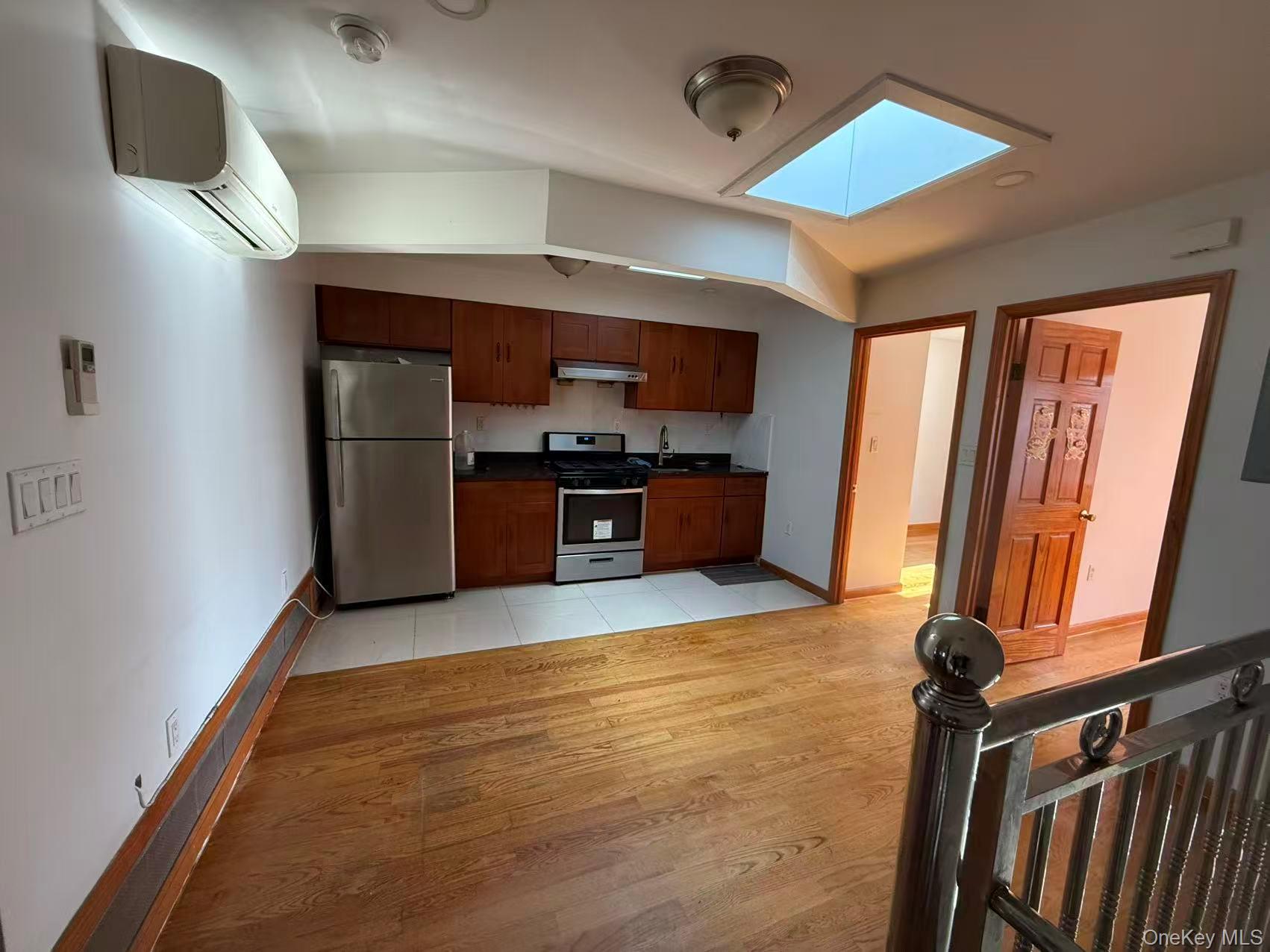 146-27 61st Road Queens, NY 11367 - Photo 3 of 17 Kitchen with a skylight, light wood finished floors, appliances with stainless steel finishes, a wall unit AC, and dark countertops