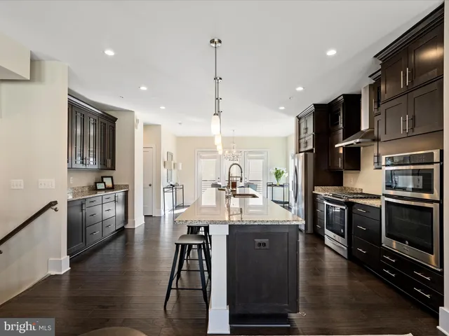 a kitchen with stainless steel appliances kitchen island granite countertop a stove top oven a sink dishwasher a dining table and chairs with wooden floor