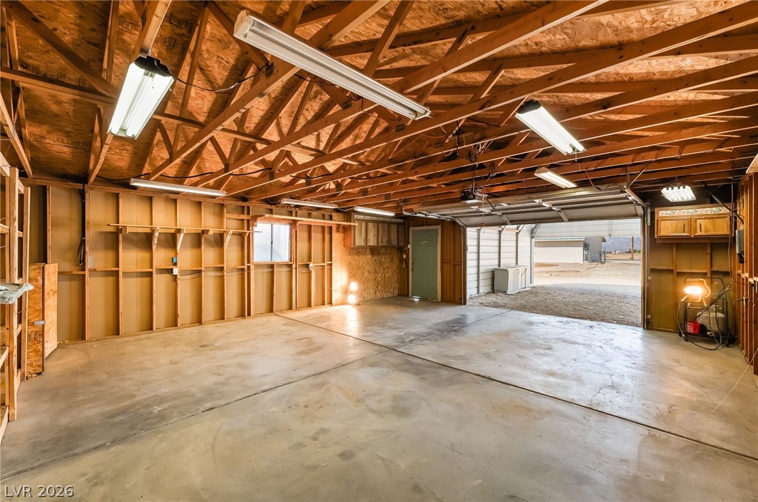 3631 South Blagg Road Pahrump, NV 89048 - Photo 1 of 47 A spacious garage with exposed beams and fluorescent lighting, offering ample room for vehicles and storage.