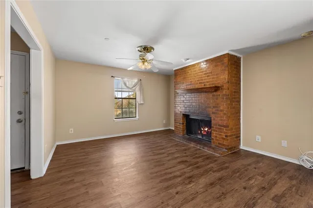 a view of an empty room with wooden floor fireplace and a window
