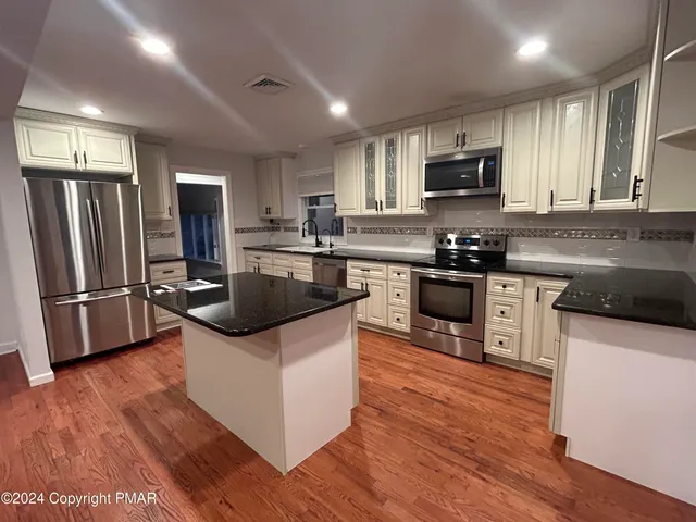 a kitchen with stainless steel appliances a stove top oven a refrigerator a sink and dishwasher with wooden floor