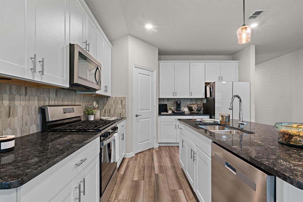 3112 Kingsgarden Road Denton, TX 76207 - Photo 12 of 38 Kitchen featuring white cabinetry, dark stone countertops, wood-finish flooring, stainless steel appliances, and a tiled backsplash