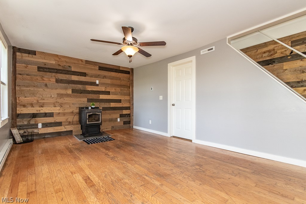 16506 Leroy Thompson Road Thompson, OH 44086 - Photo 28 of 41 Unfurnished living room with hardwood / wood-style floors, a wood stove, wooden walls, and ceiling fan