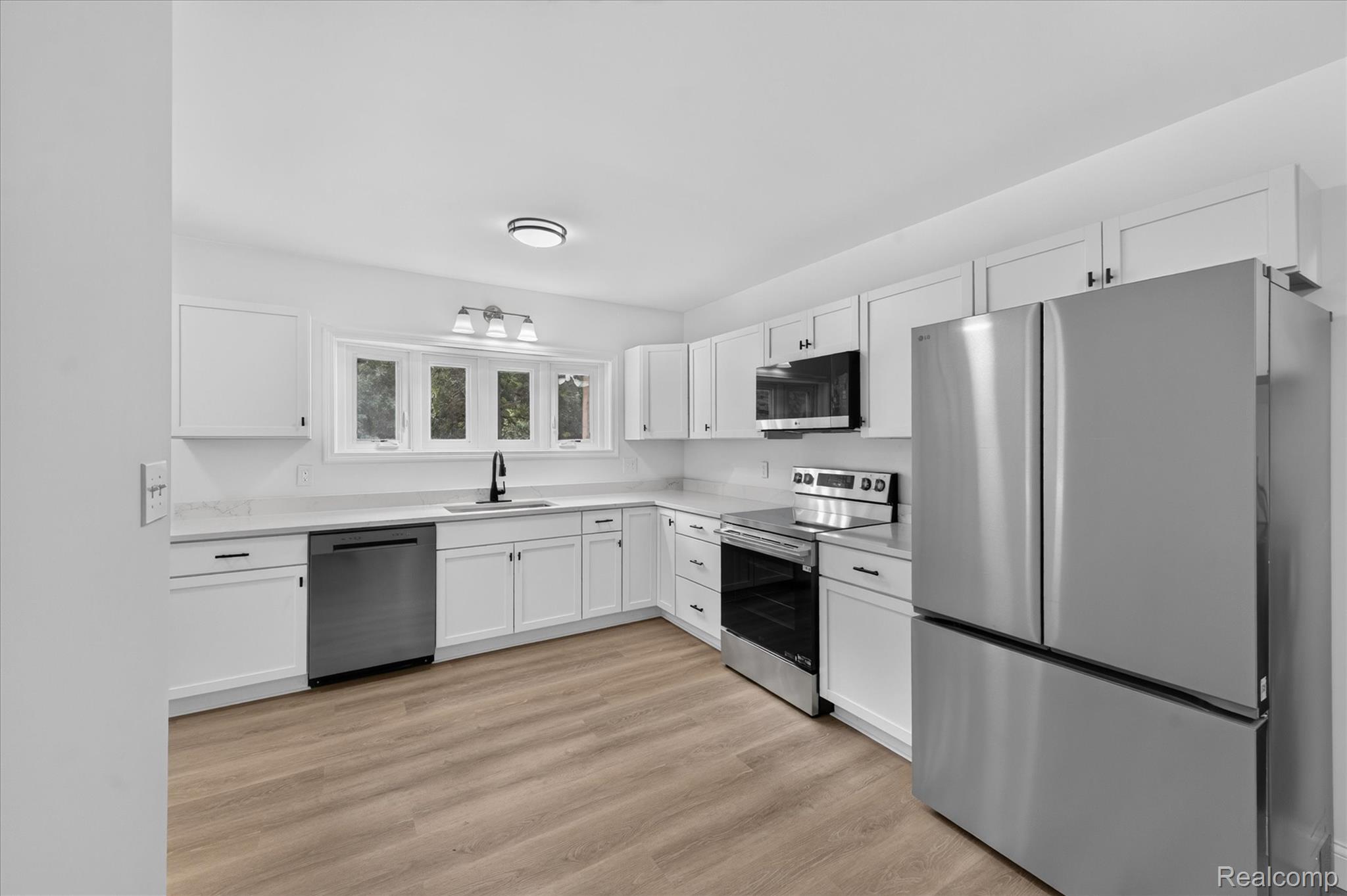 11403 White Lake Road Fenton, MI 48430 - Photo 11 of 36 White cabinetry with black hardware, stainless steel appliances, light-toned wood-finish flooring, white countertops, and a black faucet