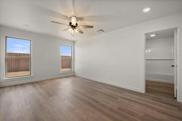 an empty room with wooden floor fan and windows
