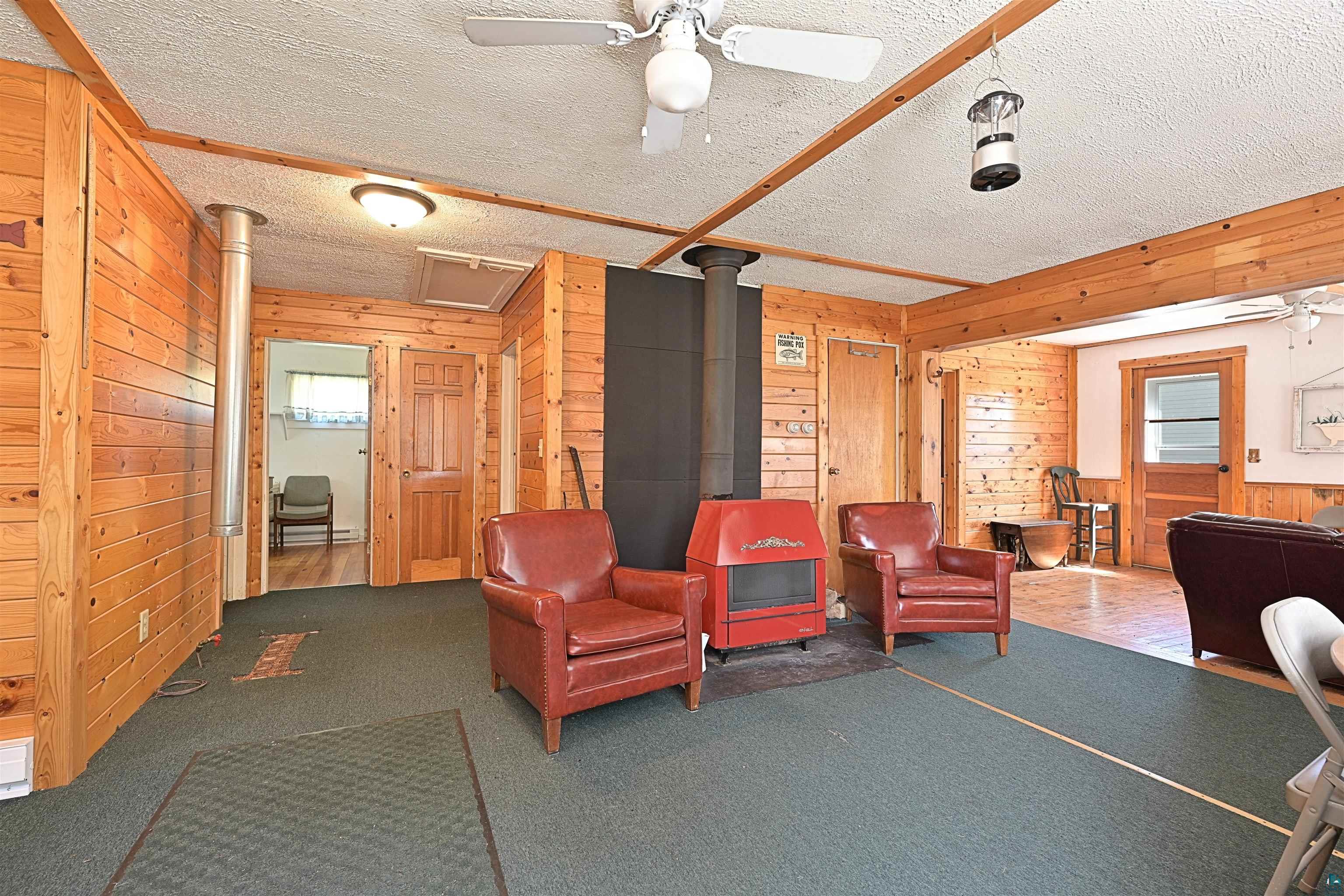 9724 State Highway 1 Isabella, MN 55607 - Photo 6 of 19 Expansive room featuring wood paneling throughout, a central red wood-burning stove with a black stovepipe, and a textured carpeted floor