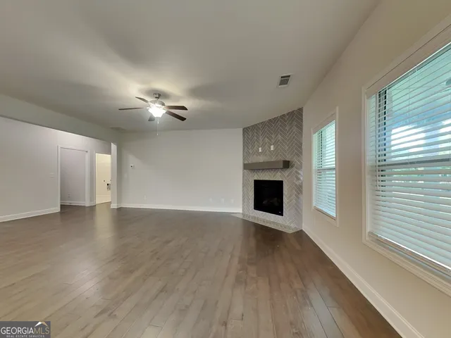 a view of an empty room with wooden floor fireplace and a window