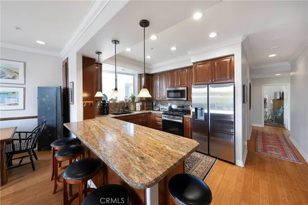 a kitchen with granite countertop a refrigerator a stove a sink a dining table and chairs with wooden floor