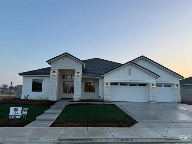 a view of a white house next to a yard with road and plants