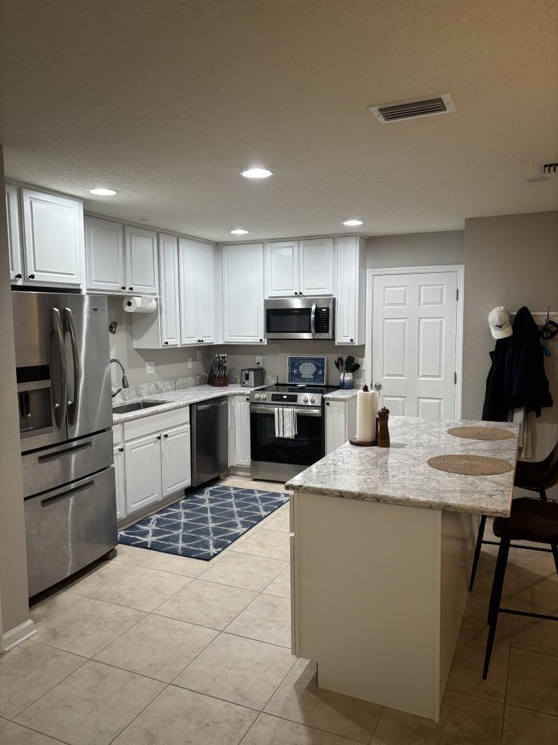 109 Islander Drive St. Augustine, FL 32080 - Photo 2 of 6 Kitchen with stainless steel appliances, light stone counters, light tile patterned floors, white cabinets, and recessed lighting