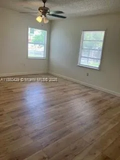 an empty room with wooden floor chandelier fan and windows