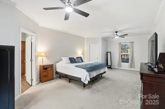 a spacious bedroom with a bed and a flat tv screen on dresser