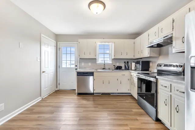 a kitchen with stainless steel appliances granite countertop a stove top oven a sink dishwasher and a refrigerator with wooden floor