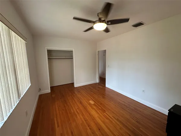 an empty room with wooden floor fan and windows