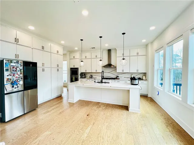a large white kitchen with kitchen island a refrigerator a stove a sink and a oven with white cabinets