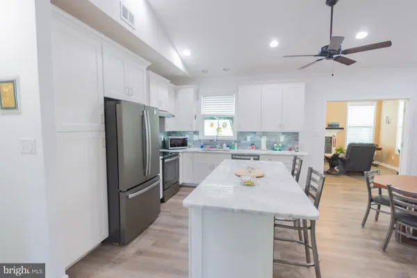 a large white kitchen with a large island oven a stove a sink a dining table and chairs with wooden floor