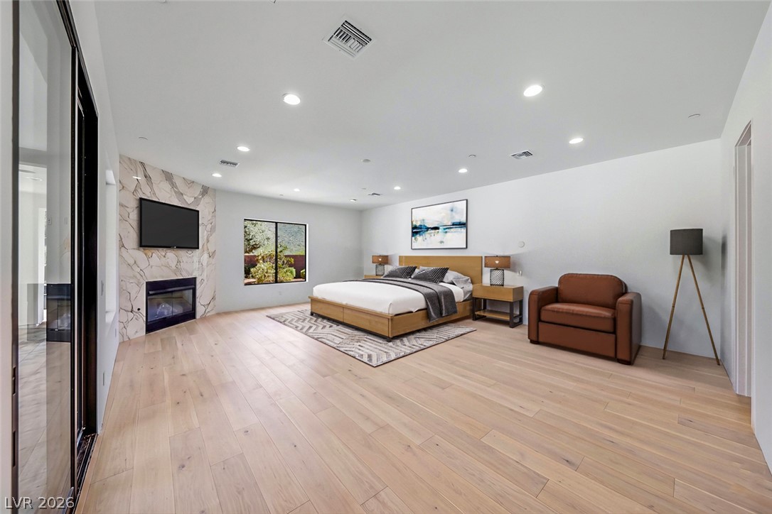 1140 Julie Road Henderson, NV 89002 - Photo 67 of 71 A spacious primary bedroom featuring a sleek fireplace with a marble-patterned accent wall and natural hardwood floors.