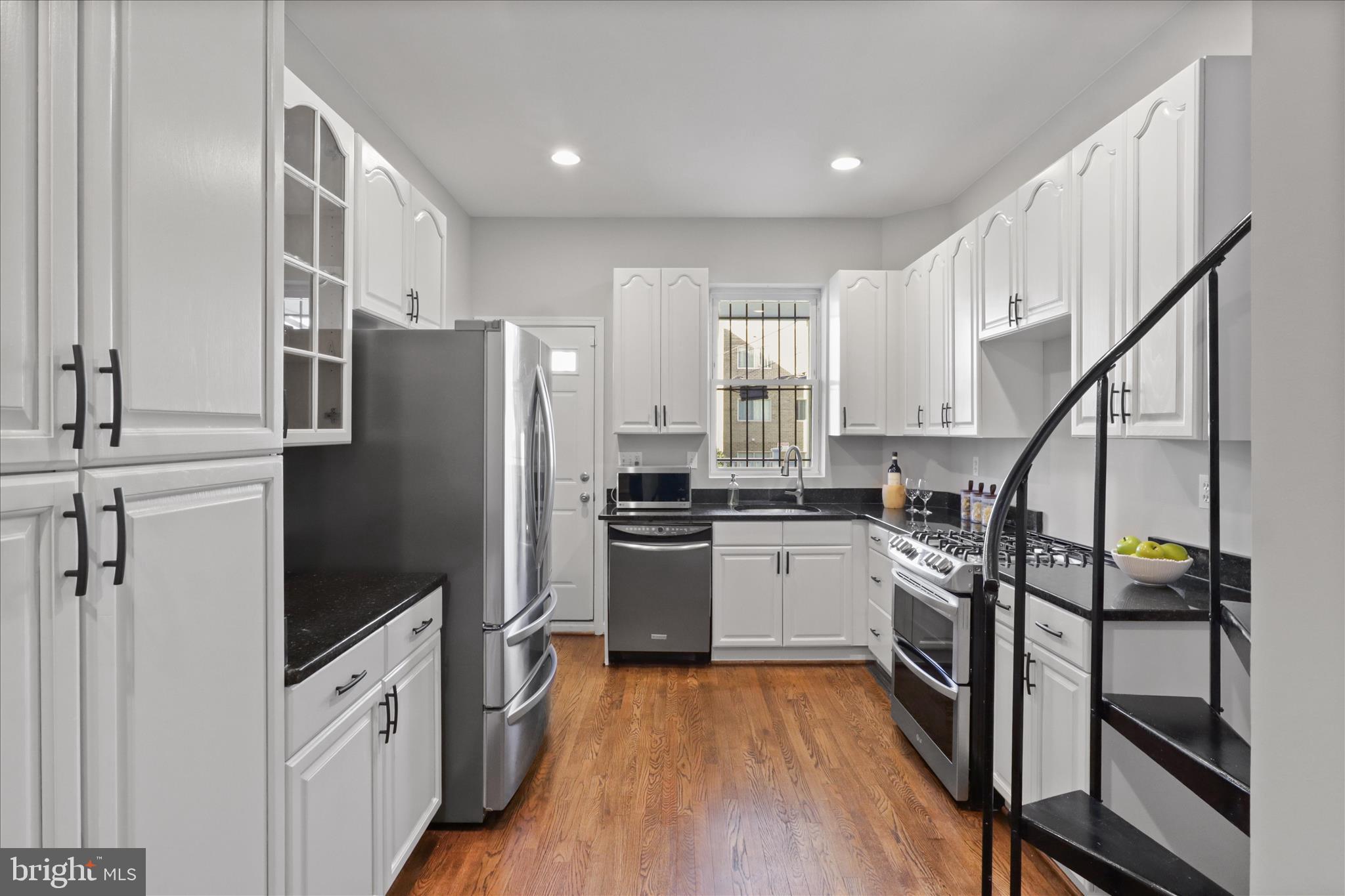 1327 Harvard Street Northwest Washington, DC 20009 - Photo 14 of 61 a kitchen with granite countertop a refrigerator a sink dishwasher a stove and white cabinets with wooden floor