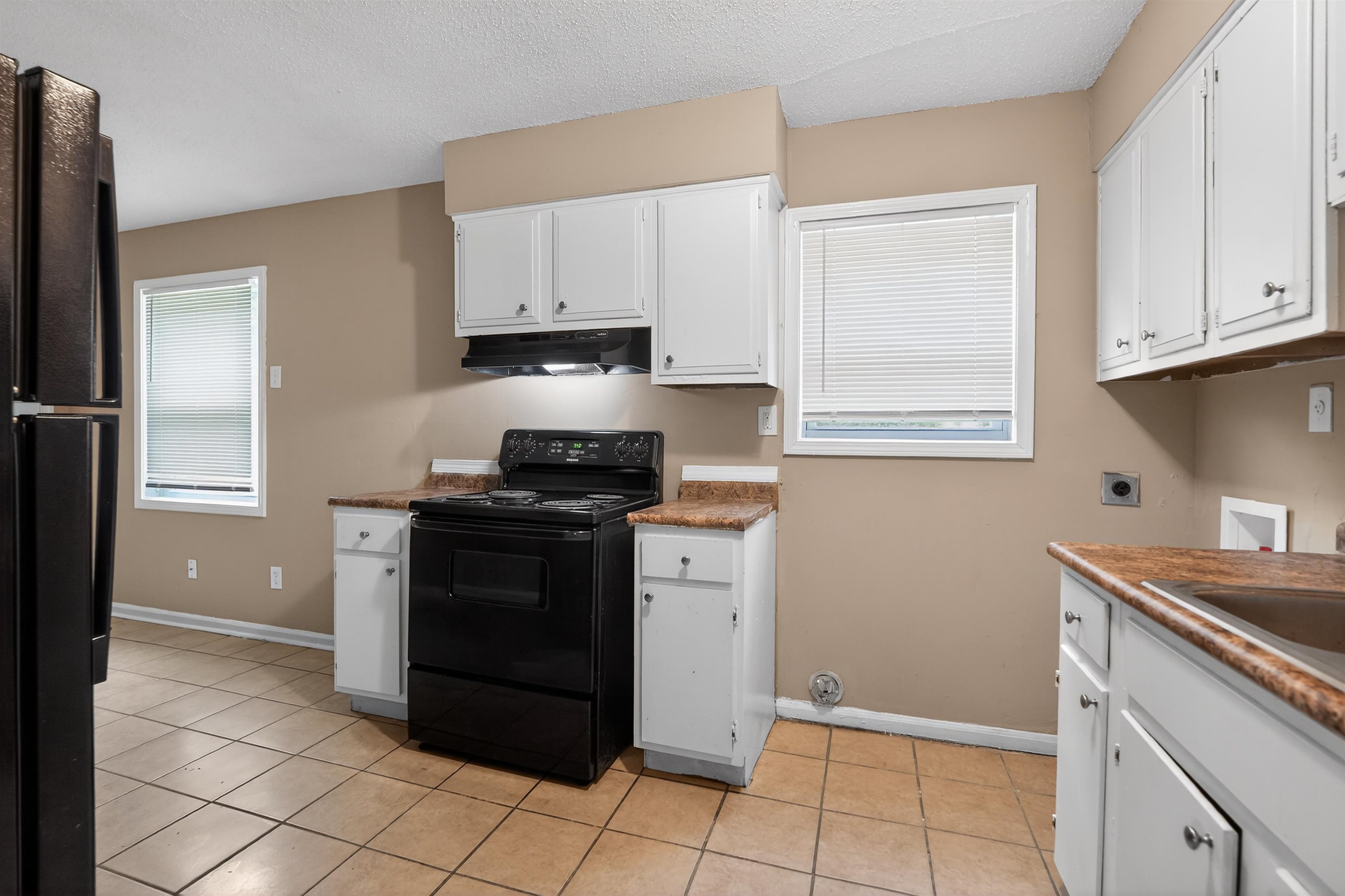 3608 Cane Ridge Drive Memphis, TN 38109 - Photo 21 of 31 Kitchen area featuring white cabinetry, a black electric range with an overhead vent, and tile flooring