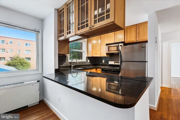 a kitchen with stainless steel appliances granite countertop a refrigerator a stove and a sink with wooden floor