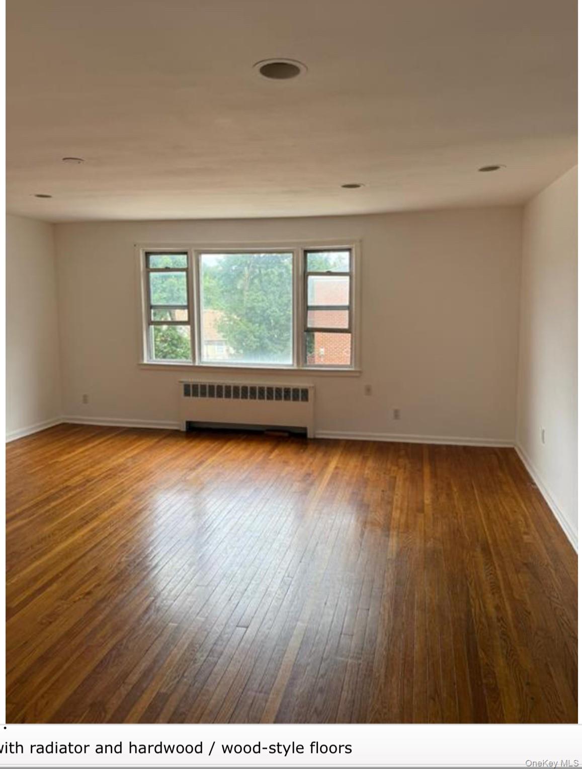 205 West Post Road, Unit 2H White Plains, NY 10606 - Photo 2 of 7 Empty room with radiator heating unit and dark wood finished floors