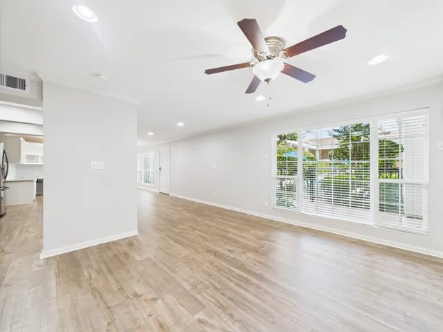 a view of an empty room with wooden floor and a ceiling fan
