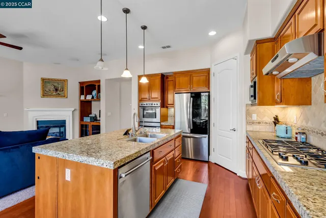 a kitchen with stainless steel appliances granite countertop a stove a sink dishwasher a refrigerator white cabinets with wooden floor and chairs