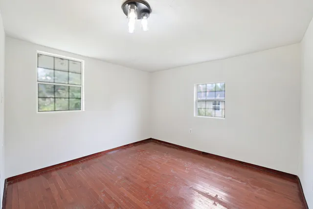 an empty room with wooden floor chandelier fan and windows