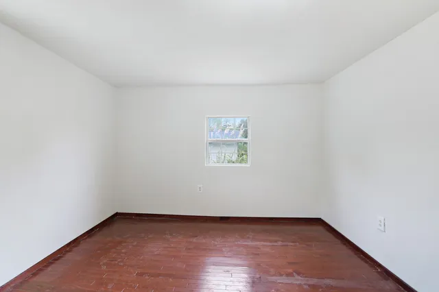 an empty room with wooden floor chandelier fan and windows