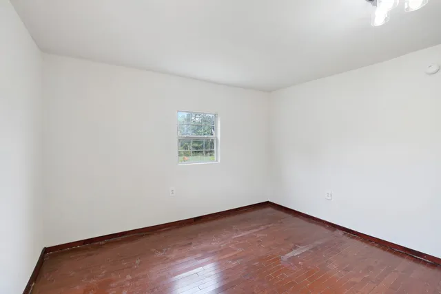 an empty room with wooden floor chandelier fan and windows