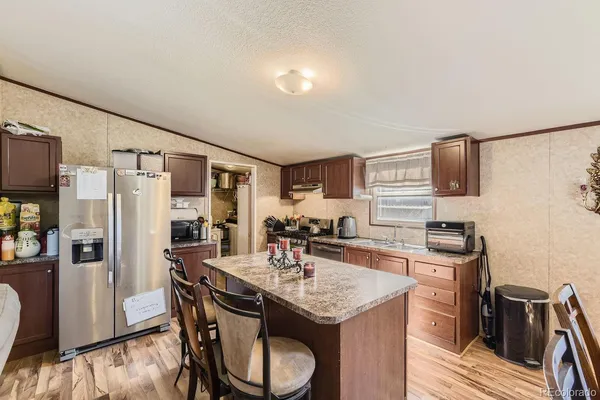 a kitchen with stainless steel appliances granite countertop a kitchen island a stove a refrigerator a sink a dining table and chairs with wooden floor
