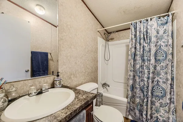 a bathroom with a granite countertop sink toilet a mirror and shower curtain