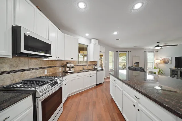 a large kitchen with granite countertop a stove top oven a sink dishwasher a dining table and chairs with wooden floor