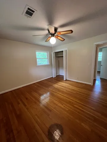 an empty room with wooden floor ceiling fan and windows